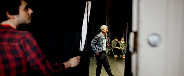 A man pulls back a curtain from the side of stage revealing someone standing on stage