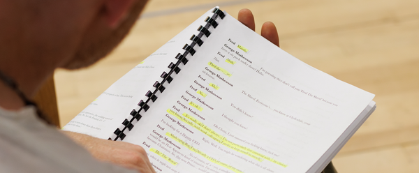 A person holds a bound script with sections highlighted in yellow.