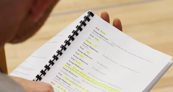 A person holds a bound script with sections highlighted in yellow.