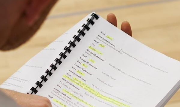 A person holds a bound script with sections highlighted in yellow.