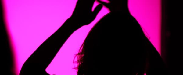 A woman silhouetted against a pink background claps her hands