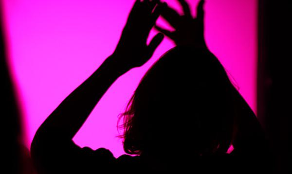 A woman silhouetted against a pink background claps her hands
