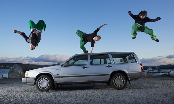 3 stunt jumpers with matching black hoodies and green joggers leaping from a car doing unique stunt poses.