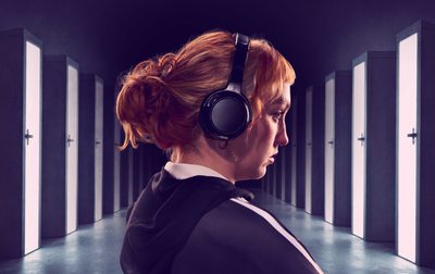 A girl wearing headphones stands in front of a corridor of doors.