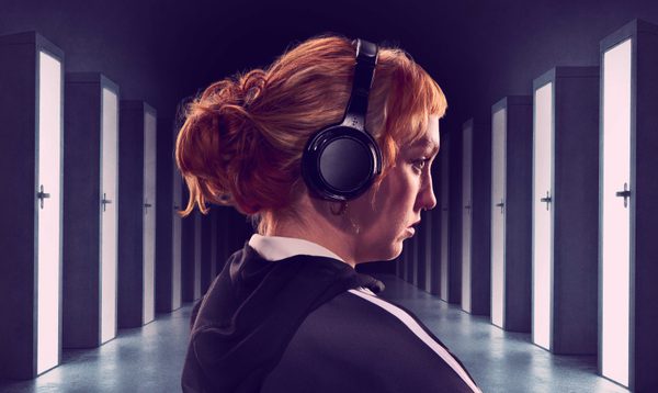A girl wearing headphones stands in front of a corridor of doors.