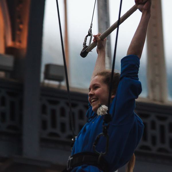 A young girl smiles as she hangs from an aerial bar.
