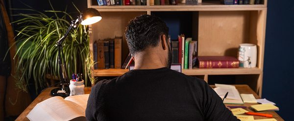 T Nazeer writes at a desk in front of a bookshelf