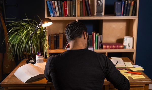 T Nazeer writes at a desk in front of a bookshelf