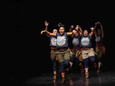 A group of people in matching khaki shorts and bleached t shirts hold their arms above their heads