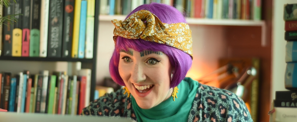 A woman in a purple wig smiling looking at a laptop screen