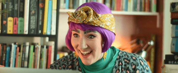 A woman in a purple wig smiling looking at a laptop screen