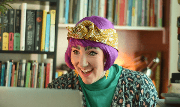 A woman in a purple wig smiling looking at a laptop screen