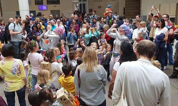 A large crowd of adults and children watching two women dressed in silver bodysuits perform