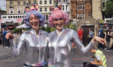 Photograph of two women in silver jump suits and pastel wigs