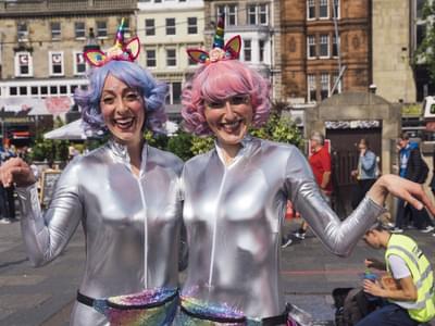 Photograph of two women in silver jump suits and pastel wigs