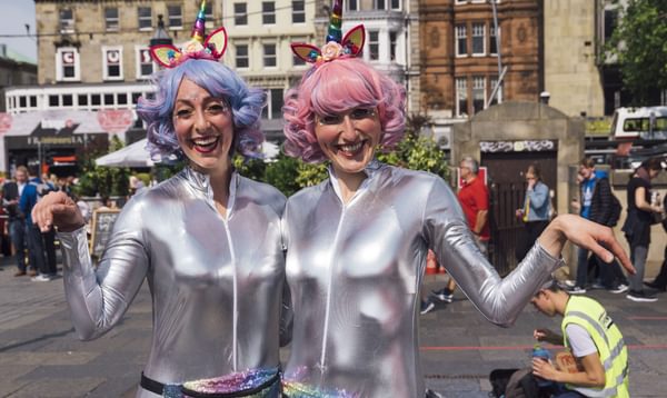 Photograph of two women in silver jump suits and pastel wigs