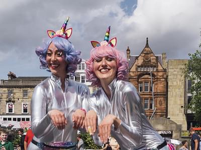 Two women dressed in silver body suits with pastel coloured hair and unicorn horns
