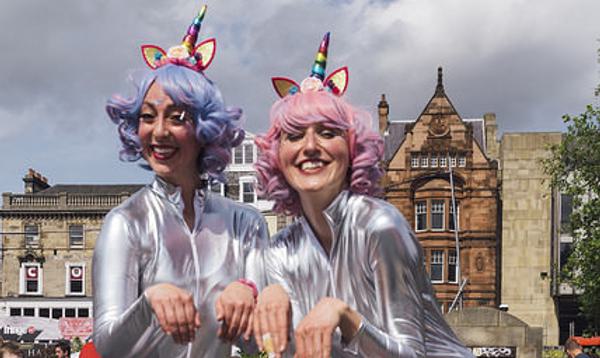 Two women dressed in silver body suits with pastel coloured hair and unicorn horns