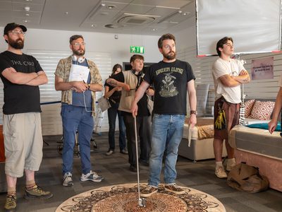Audience members stand in a bed shop watching something off-camera