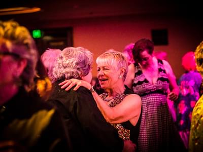 A photograph of two older women dancing together on a busydance floor.