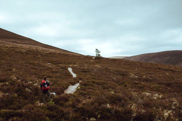 A person following a mountain path, towards hills on the horizon