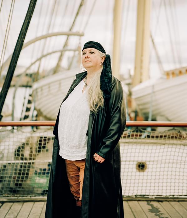 Woman in long leather jacket and bandana in front of ship