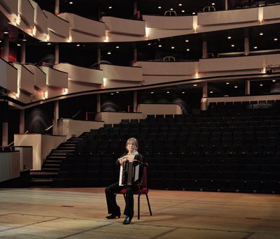 An accordionist sitting on a chair in a concert venue