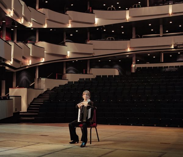 An accordionist sitting on a chair in a concert venue
