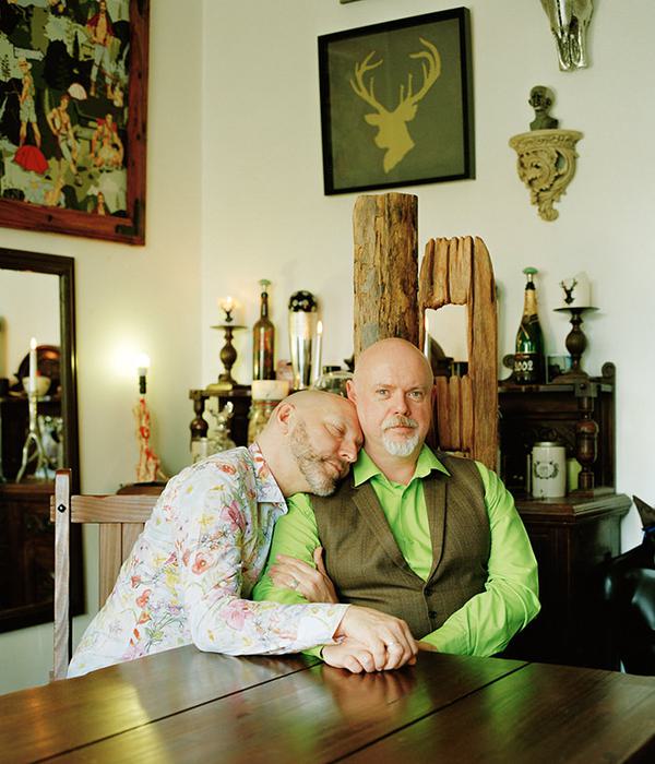 Two men sat at a homely table holding hands