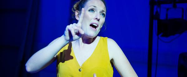 White woman in yellow dress, pointing finger upwards