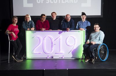 A group of people gathered around a neon sign that says '2019'