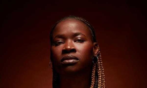 A photograph of Adura Onashile on a dark red background.