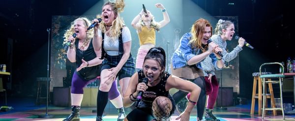 Six young women yelling into microphones