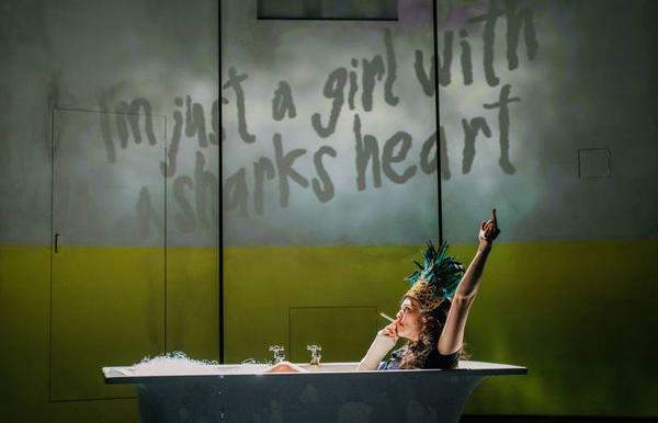 'I'm just a girl with a sharks heart' is written on the wall, a woman sits in the bath smoking and bearing her middle finger