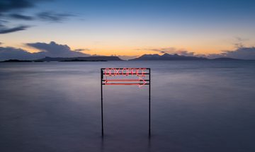 A neon box office sign that points to the right. Behind it a vast misty landscape