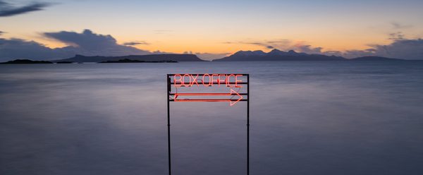 A neon box office sign that points to the right. Behind it a vast misty landscape