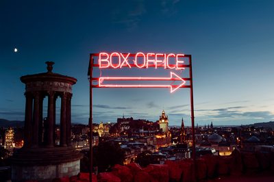 A neon box office sign in front of a view of Edinburgh at dusk from Calton Hill