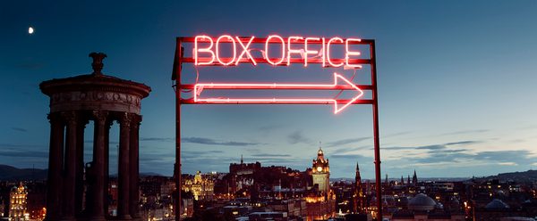 A neon box office sign in front of a view of Edinburgh at dusk from Calton Hill
