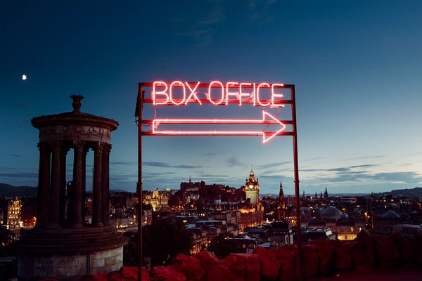 A neon box office sign with a view of Edinburgh at dusk behind.