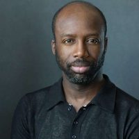 Jo Servi looks at the camera intently yet sincerely. He sits in front of a grey background.