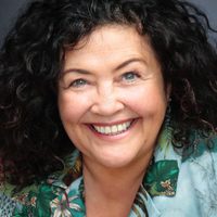 Mandi Symonds beams at the camera, she has dark curly hair and wears a trendy jungle print top.