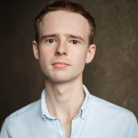 Aron Dochard gazes at the camera. He wears a pale blue shirt.