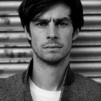 Black and white, Dyfan has dark hair and watches the camera intently