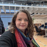 A selfie of Sam in an office, she has brown hair and a colourful scarf.