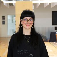 Phoebe has long black hair and glasses, she smiles at the camera.
