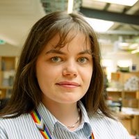 Lizzie smiles at the camera. She has long brown hair and wears a stripey shirt.