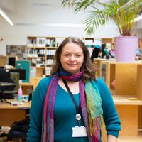 Sam smiles at the camera, she wears a colourful scarf