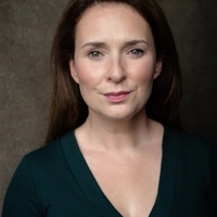 Jo looks at the camera. She has dark hair and wears a dark green top.