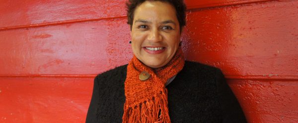 A woman with short hair smiling in front of a red background