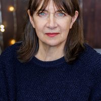 Maureen looks intensely at the camera. Her hands are clasped.
